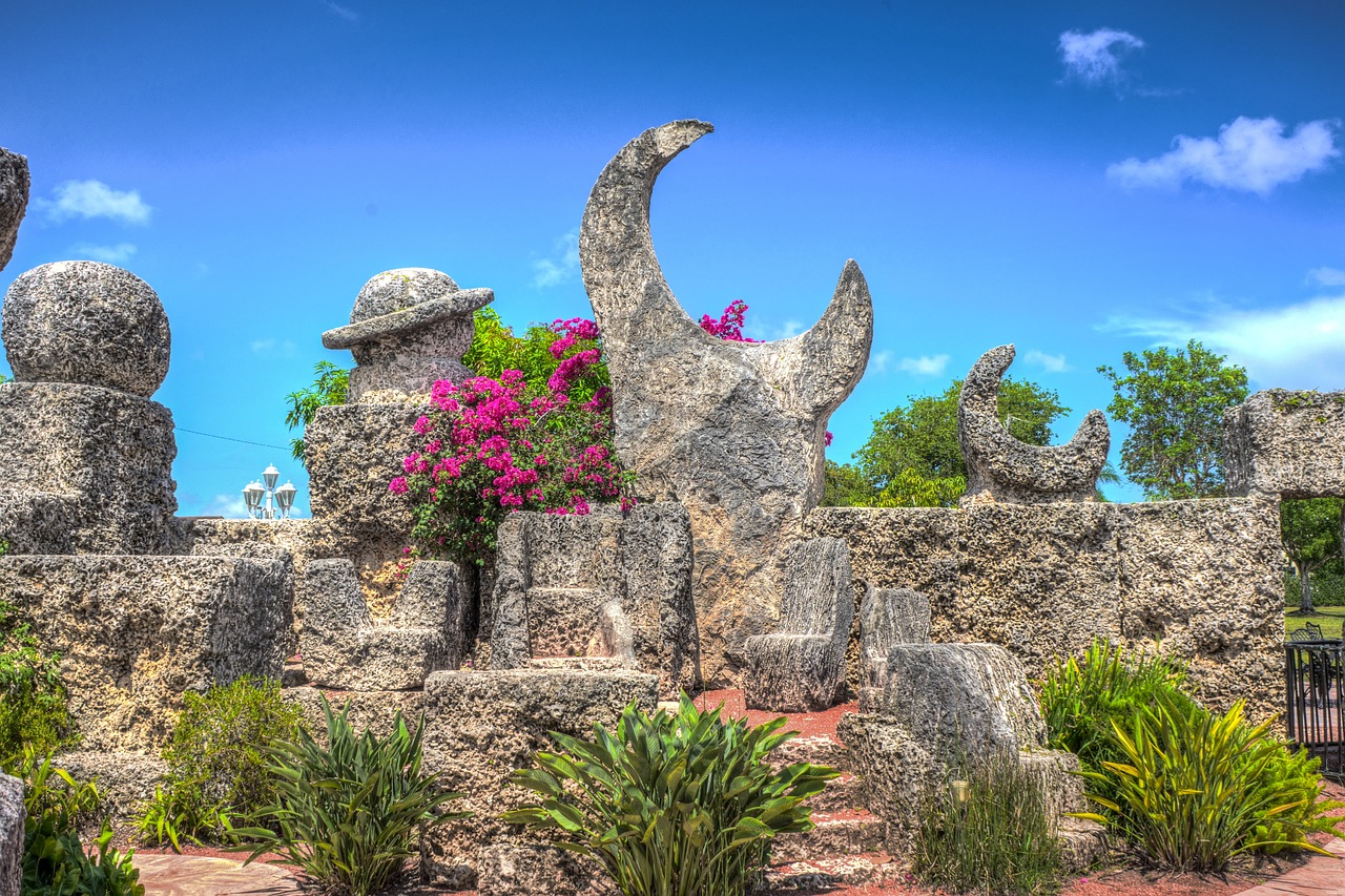 a large stone statue in a garden with Coral Castle in the background