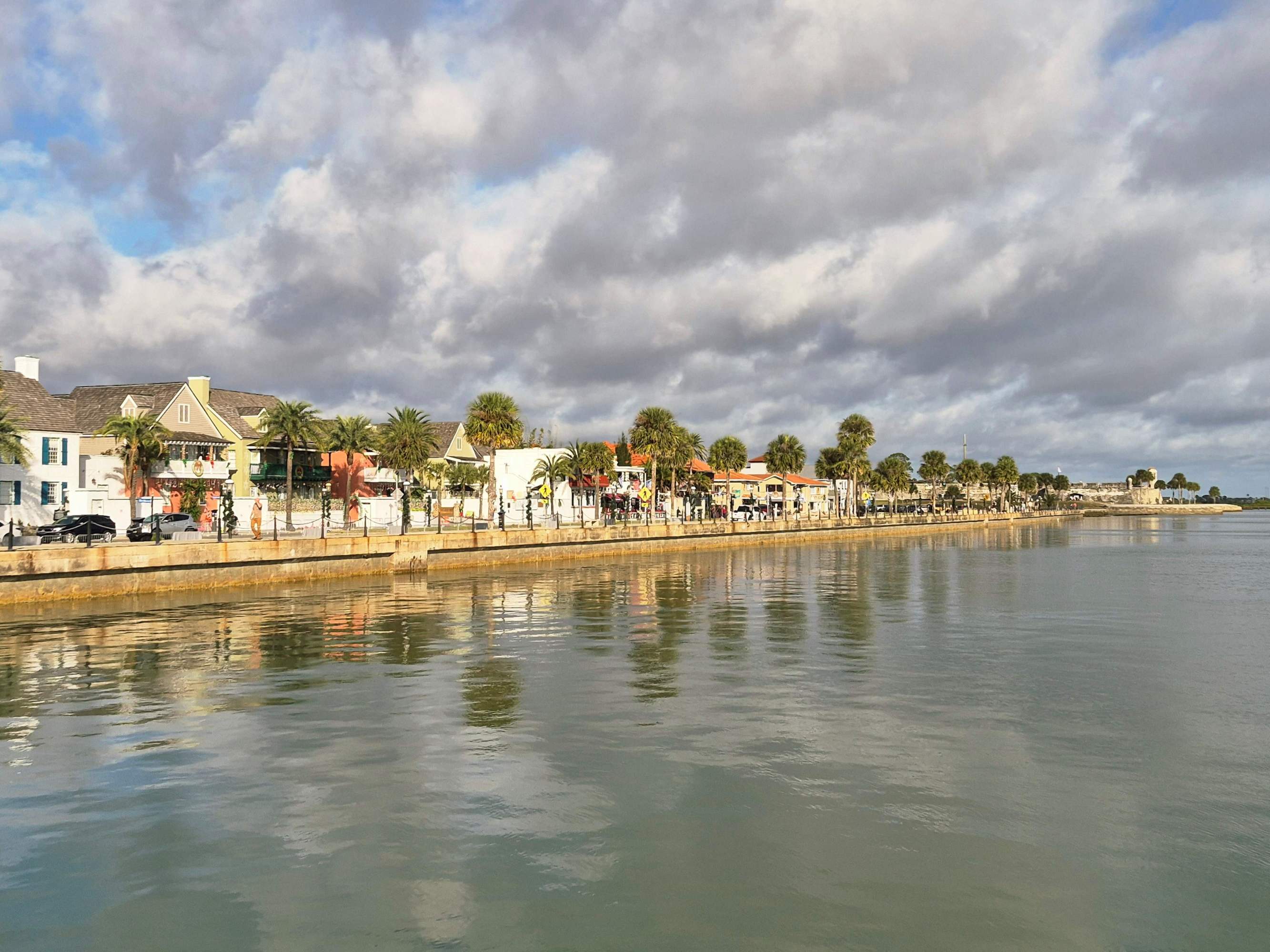 Waterfront lined with colorful buildings and palm trees under a cloudy sky.