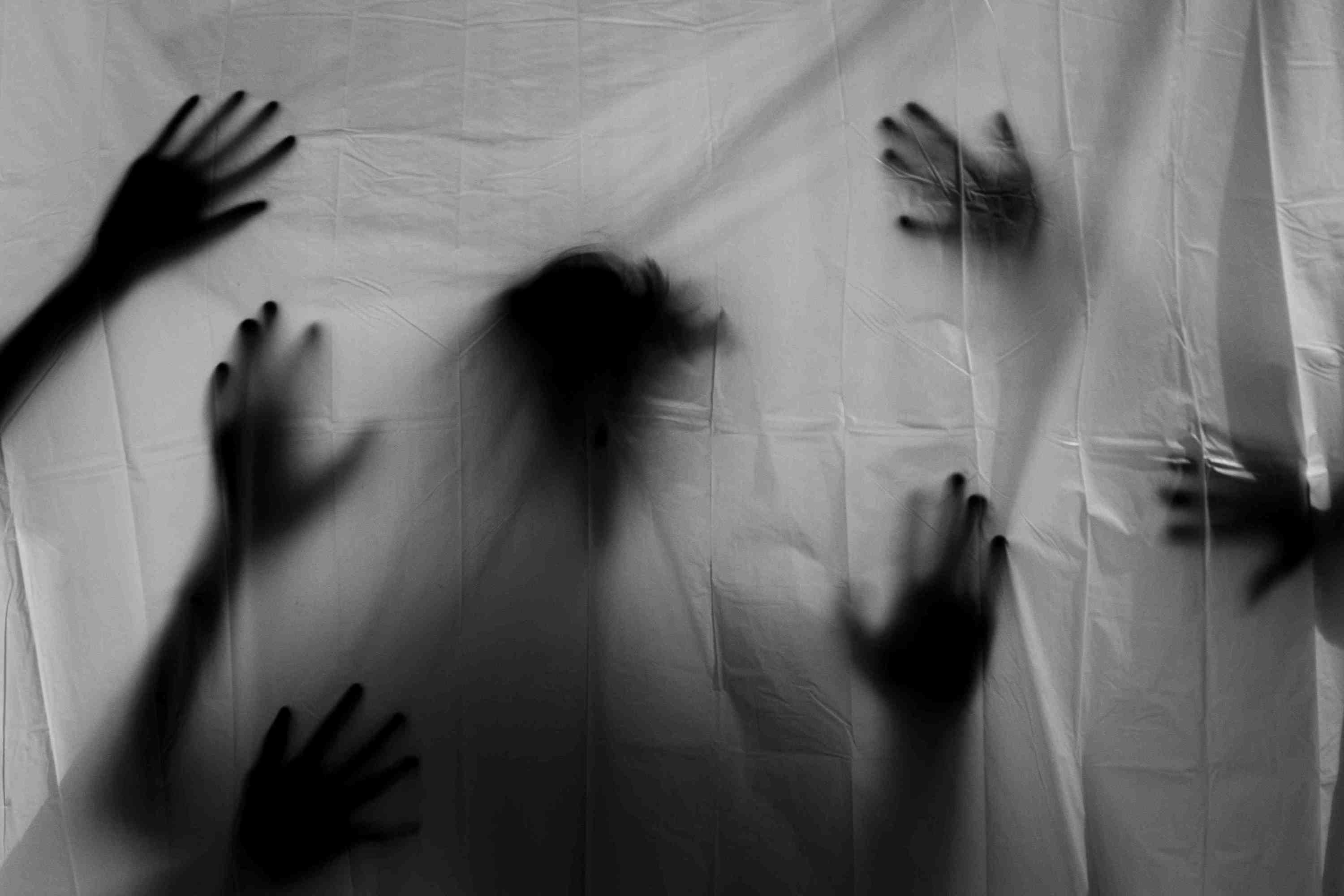 Silhouettes of hands and a head pressing against a translucent sheet.