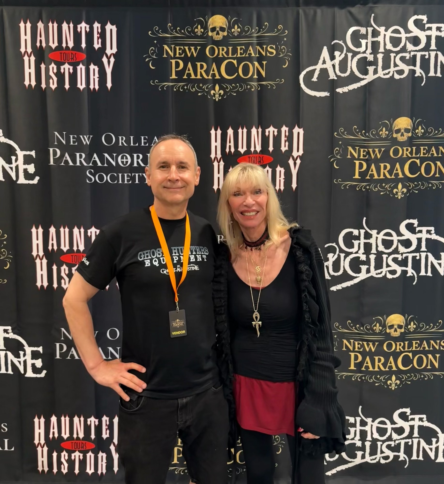 Two people posing at a paranormal convention backdrop.